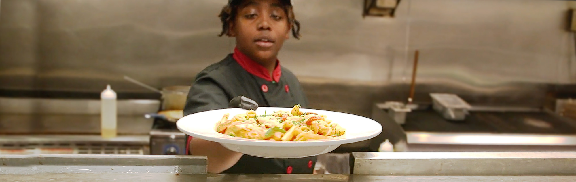 Chef hands plate of pasta from kitchen to server.